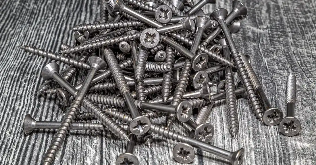 Pile of stainless steel screws on a weathered wood surface