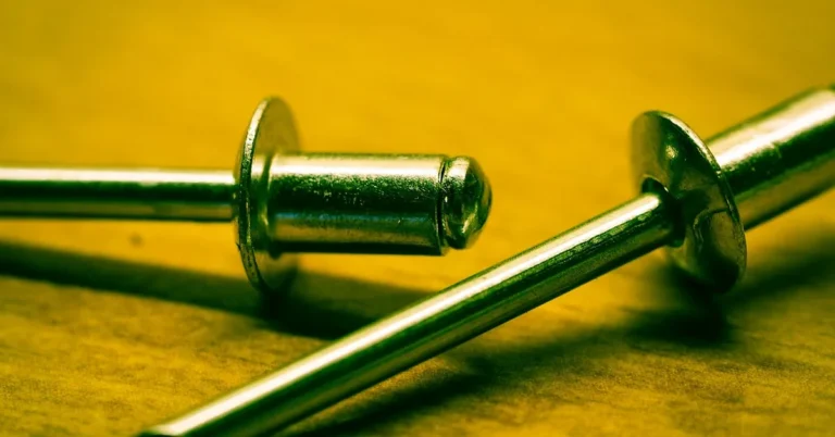Two aluminum blind rivets lying on a wooden surface