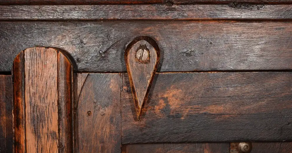 Close-up of dark aged wood cabinet panels with a carved pull