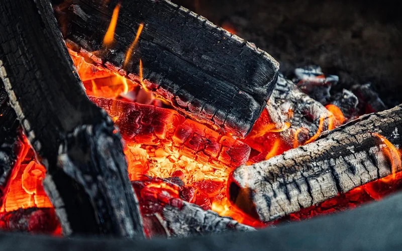 Wood point being fire-hardened by rotating it just above glowing campfire embers