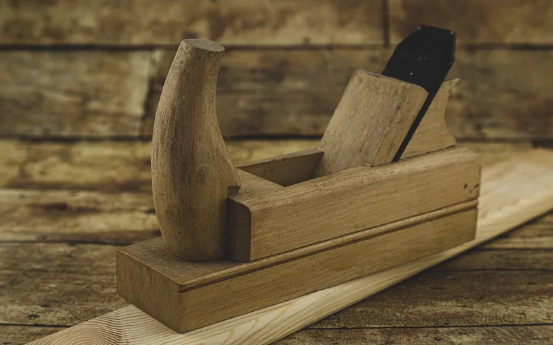 wooden hand plane resting on a board used to smooth wood after paint removal