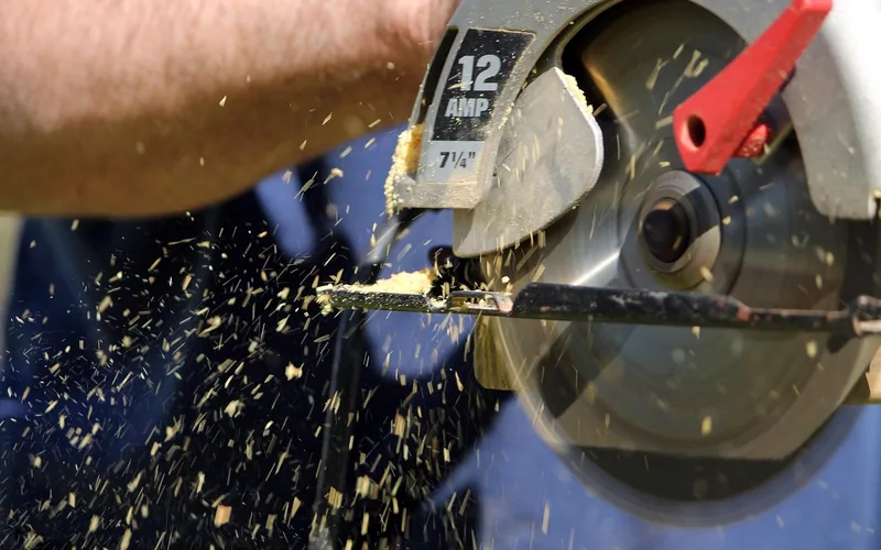 handheld 7 1/4 inch circular saw cutting through wood with sawdust flying