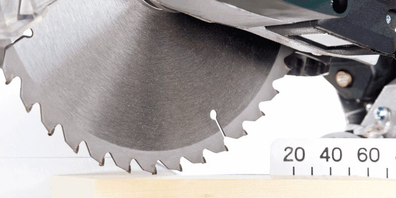 Close-up of a miter saw carbide-tipped blade with the angle scale visible behind it