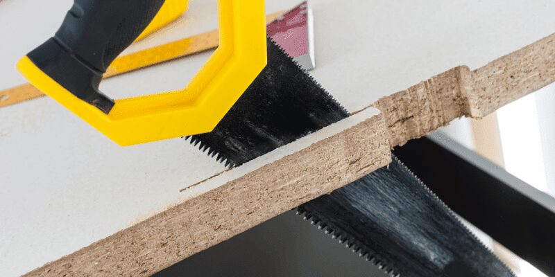 close-up of a hand saw blade cutting through particleboard countertop substrate