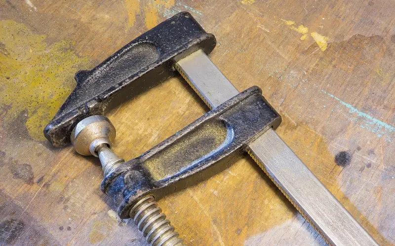 metal F-clamp holding a wood board against a workbench during glue-up