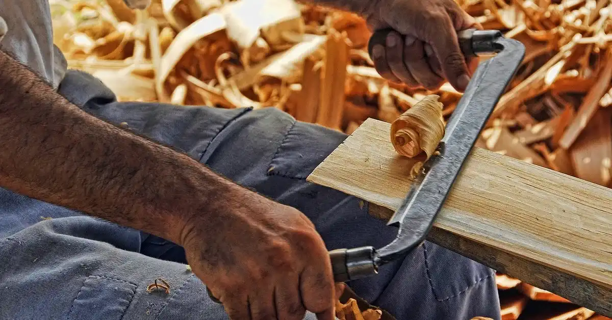 Woodworker using a drawknife to shape a wood plank, the kind of precision hand control that also matters when marking wood with a mechanical pencil