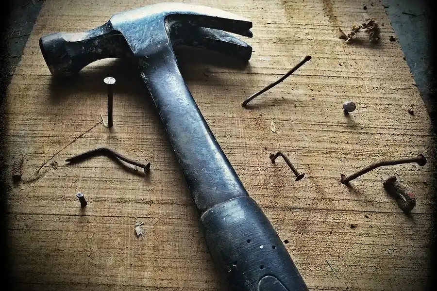 Hammer and nails on a rough-sawn wood board in a carpentry workshop Hammer and nails on a rough-sawn wood board in a carpentry workshop