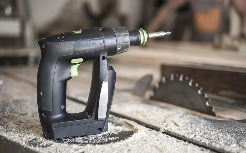 Cordless drill resting on a dusty table saw next to the blade insert