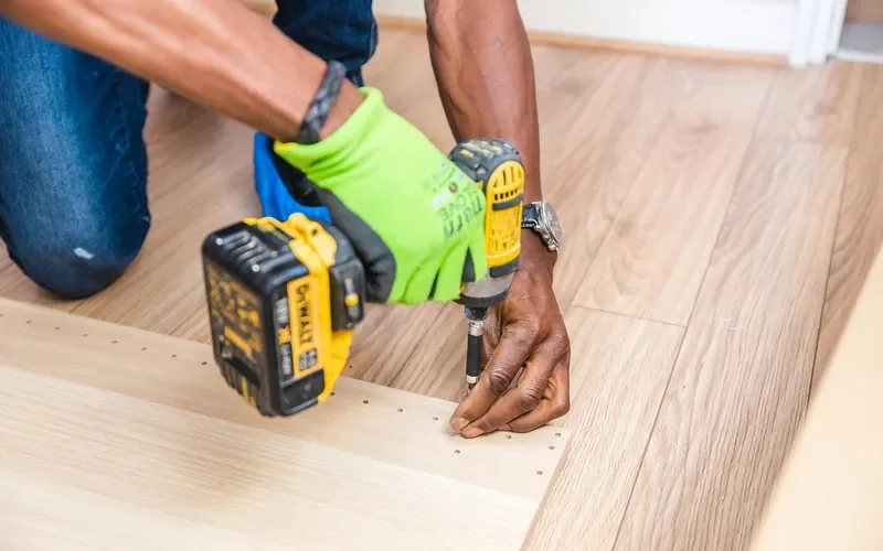 carpenter drilling a pre-drilled pilot hole into a laminated particleboard panel before driving a confirmat screw carpenter drilling a pre-drilled pilot hole into a laminated particleboard panel before driving a confirmat screw