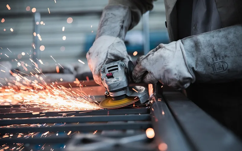 gloved hands guiding a power cutting tool through a steel frame, sparks flying near the blade guard