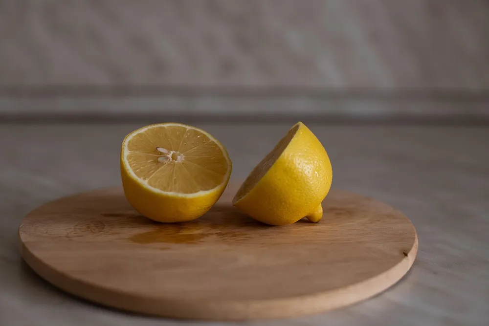 Lemon halves on a bare round wooden board with a juice spot soaking in