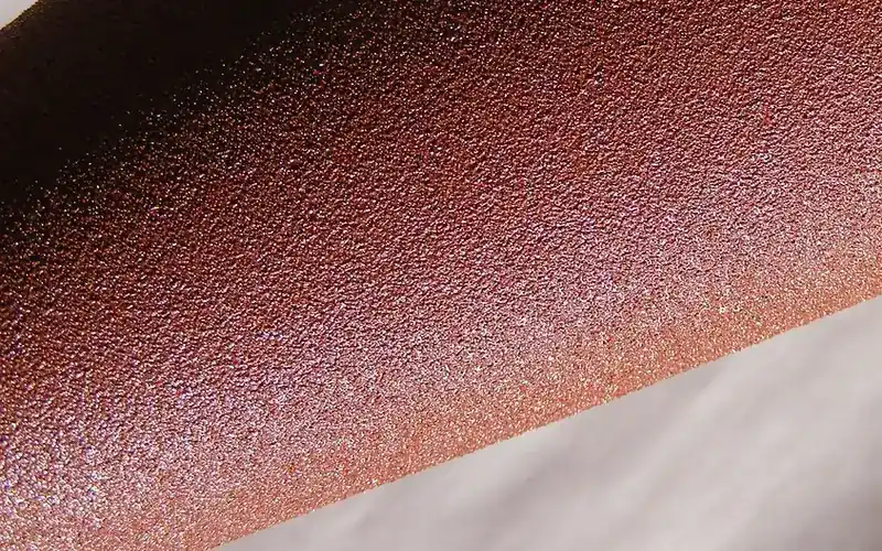Close-up of the abrasive grain surface on a sheet of red-brown coated sandpaper Close-up of the abrasive grain surface on a sheet of red-brown coated sandpaper