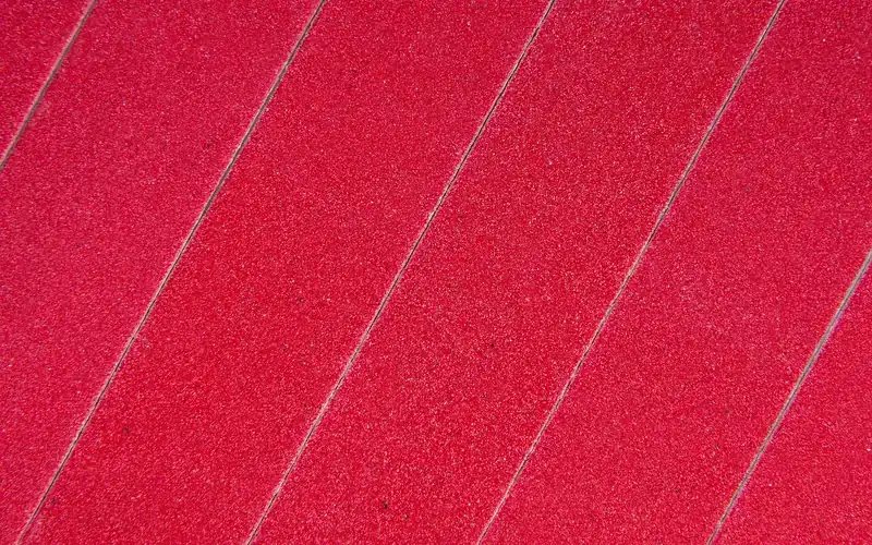 Red coated abrasive strips with fine even grit under direct light Red coated abrasive strips with fine even grit under direct light