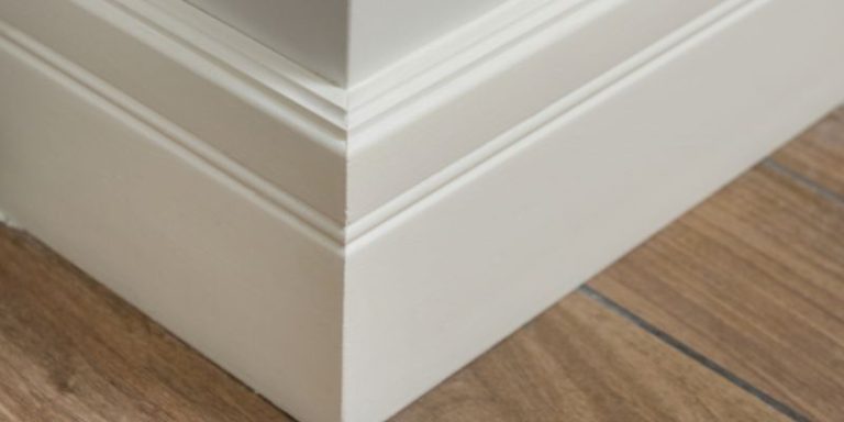 Mitered outside corner of painted two-step baseboard meeting on a wood-look floor
