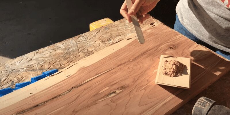 hand sanding a wood board with a small pile of collected sawdust nearby
