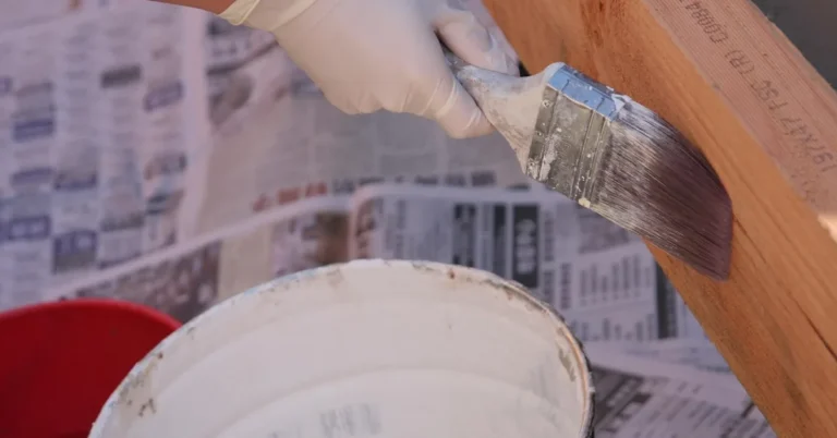 gloved hand brushing wood bleach lightening solution onto a wood plank over a bucket