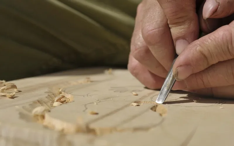 Woodcarver cutting a pattern into a light-colored wood board with a gouge
