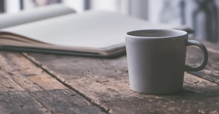 White ceramic mug on a worn wooden table, the kind of setup that leaves water rings