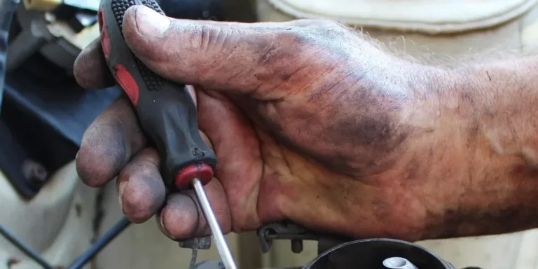 Mechanic adjusting a small-engine carburetor screw with a screwdriver