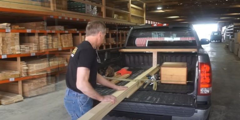 lumber yard employee loading a long board into a pickup truck bed