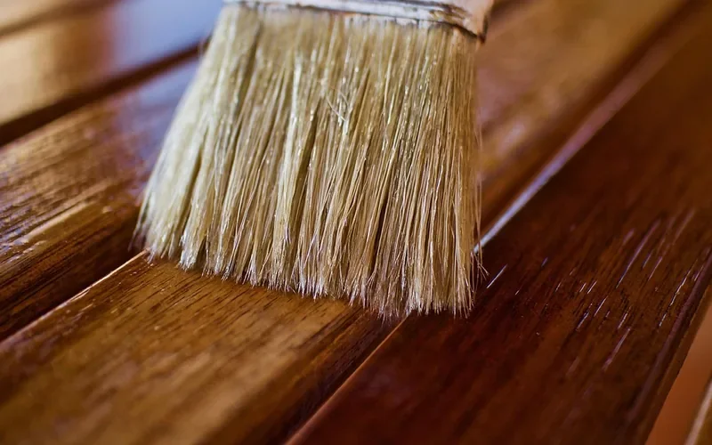 Bristle brush spreading a glossy clear coat over stained wood Bristle brush spreading a glossy clear coat over stained wood