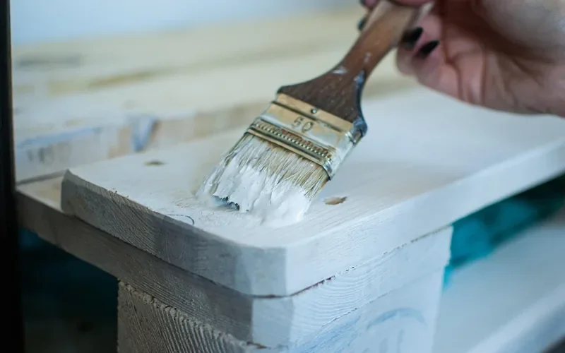 Hand brushing a white coat of paint onto a wooden board Hand brushing a white coat of paint onto a wooden board