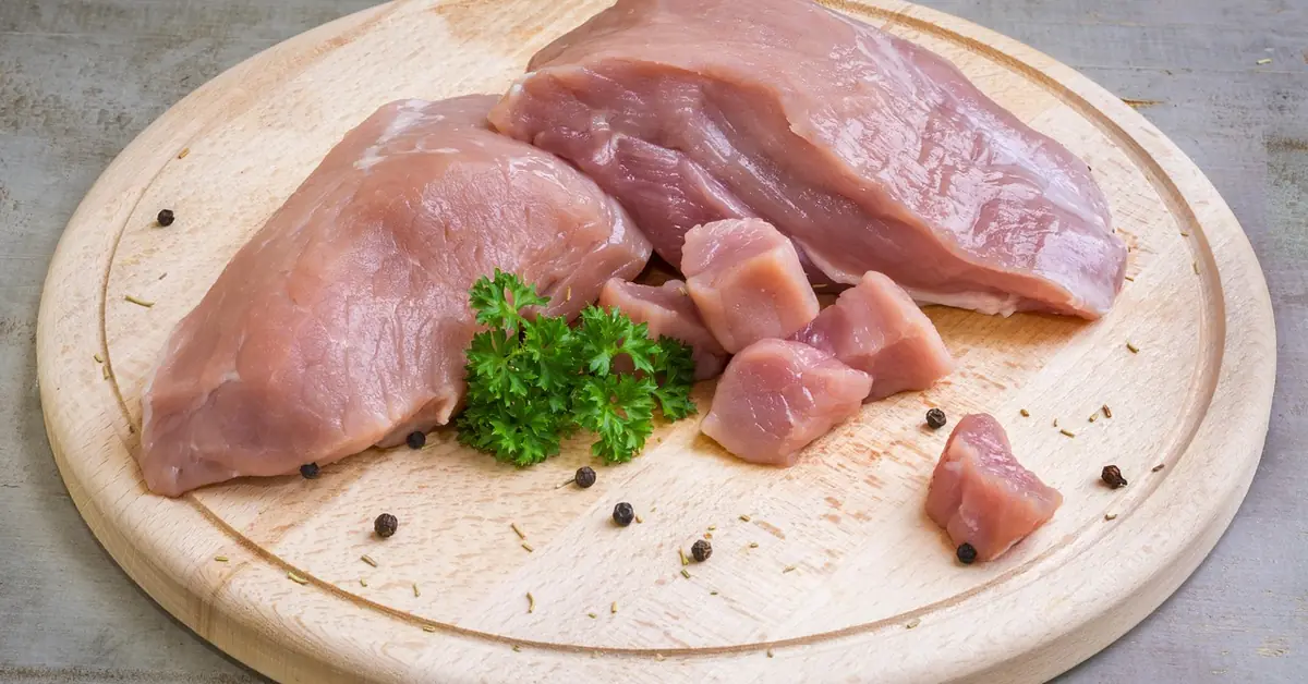 raw meat cuts resting on a wooden cutting board with parsley and peppercorns