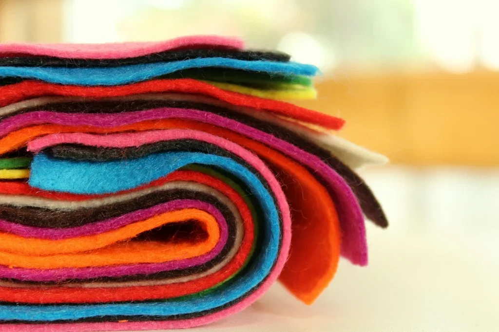 Stack of colorful felt fabric sheets ready to be cut and glued onto wood