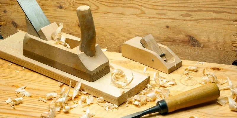A wooden jack plane and block plane on a workbench surrounded by curled wood shavings