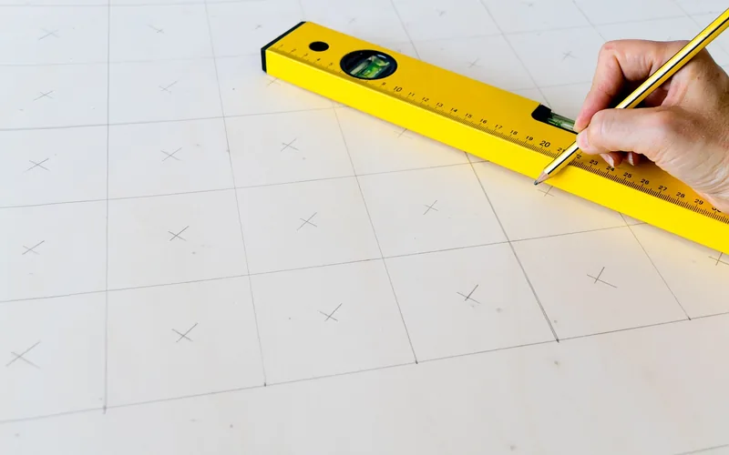 marking measurements on a wood board with a yellow level and pencil