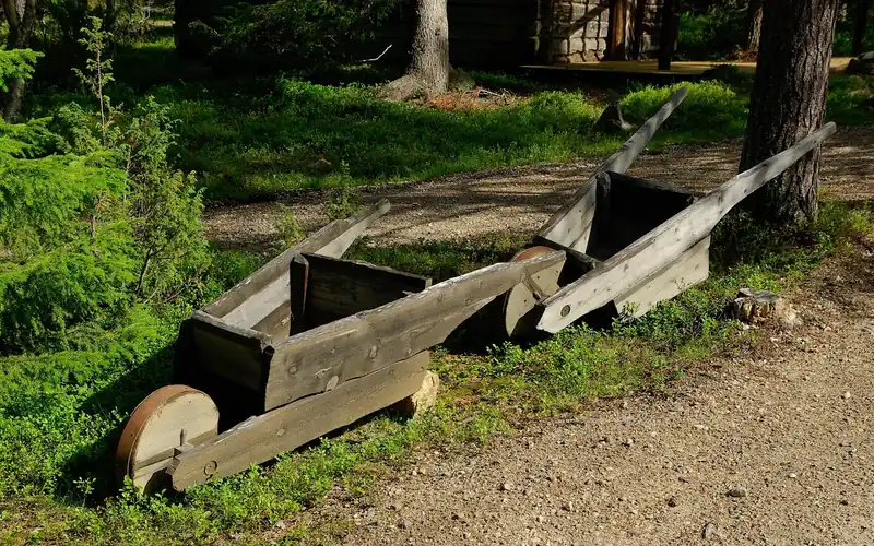 pair of old all-wood wheelbarrows with wood handles and wood wheels sitting outdoors