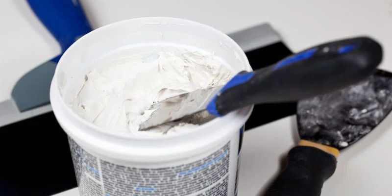 A tub of spackle with putty knives ready for application