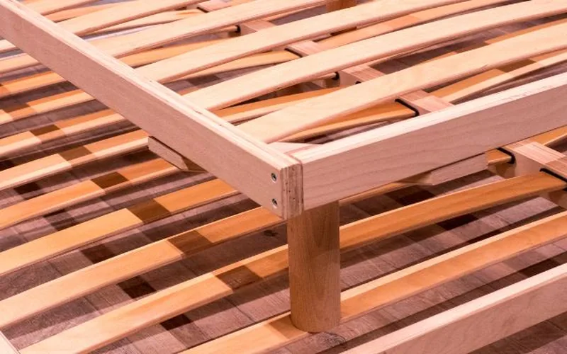 close-up of a solid wood bed frame corner joint with slats and a center support leg