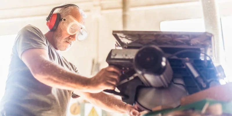 Woodworker wearing safety glasses and ear protection operating a miter saw