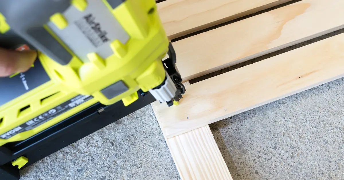Pneumatic finish nailer driving a nail into wood slats close up