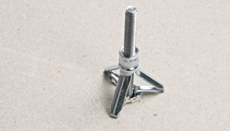 Butterfly screw anchor toggle bolt with wings extended resting on a drywall sheet