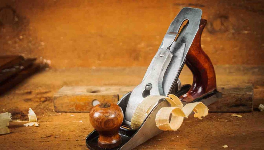 hand plane resting on a workbench with wood shavings curling off the freshly installed blade