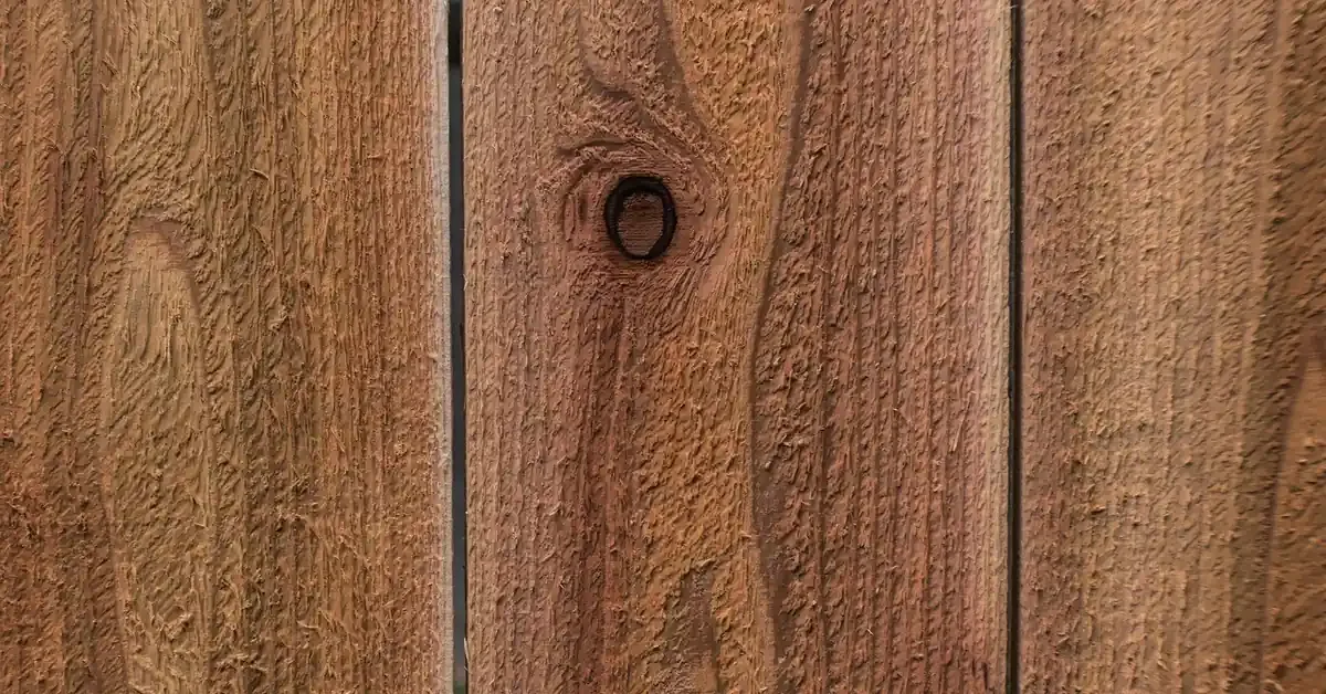 Rough-sawn cedar fence boards with a warm reddish-brown finish and a visible knot