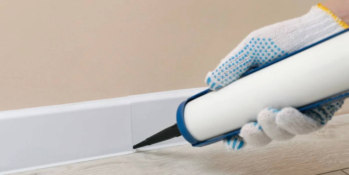 painter using a small brush to paint over a caulked baseboard seam