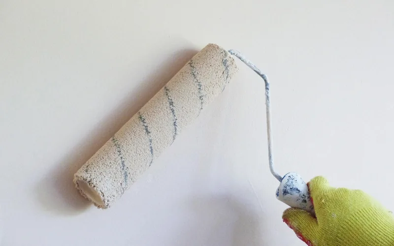 painter applying interior latex paint to a wall with a roller