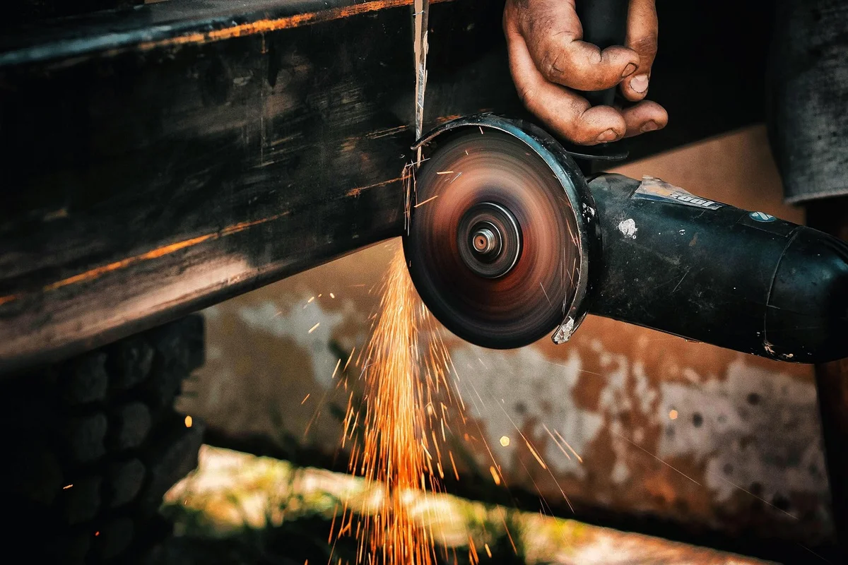 Angle grinder with a flap disc removing rust and mill scale from a steel beam before painting