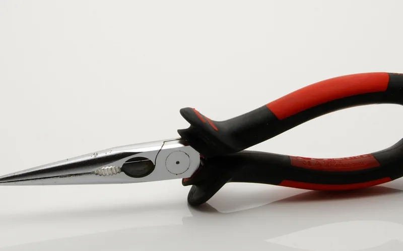 Needle-nose pliers gripping a metal staple for removal from hardwood floor