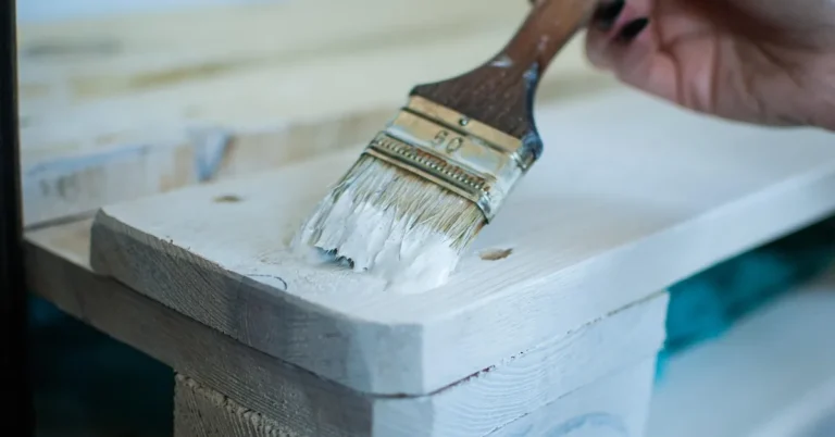 hand applying white primer with a paintbrush to a bare wood board