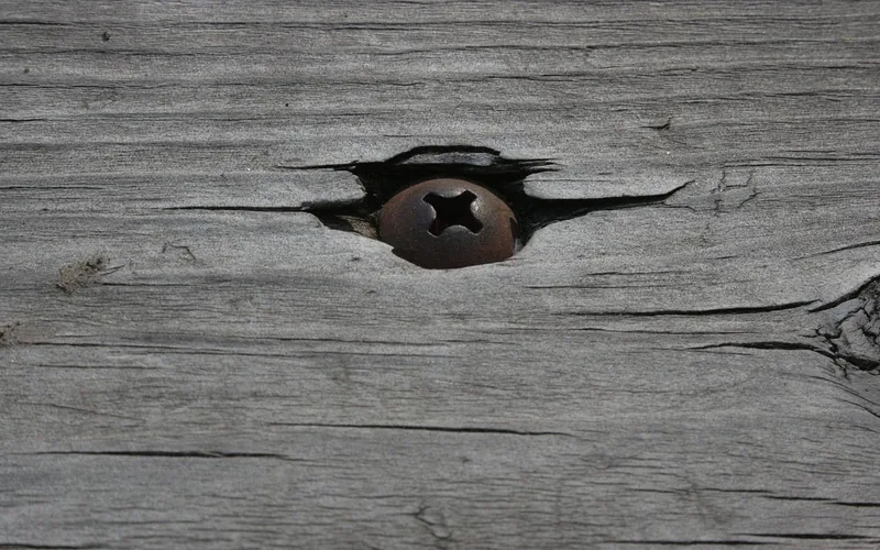 Rusted Phillips screw head sitting in weathered wood