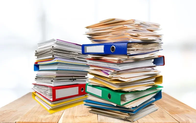 Stack of binders and folders holding purchase records on a wooden table