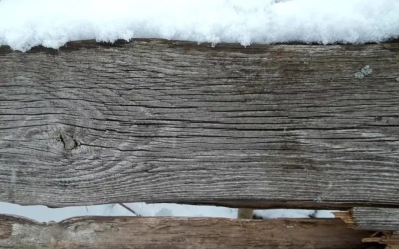 Weathered wooden fence rail topped with snow in cold weather