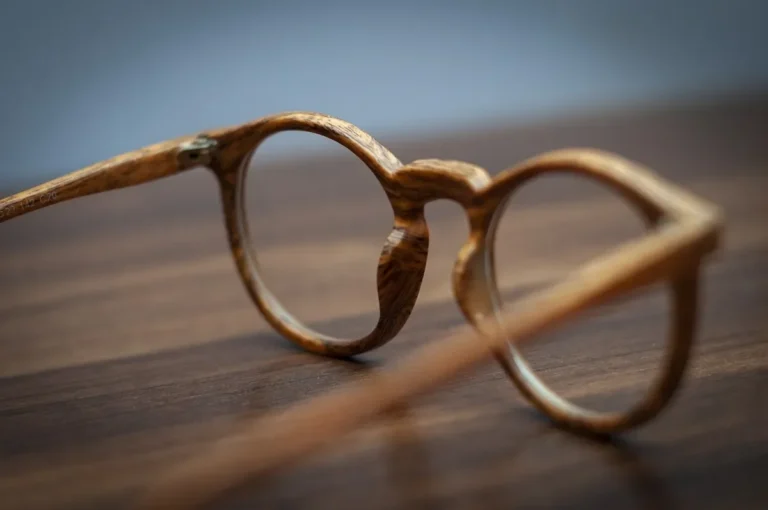 Round eyeglasses with a wood-grain frame resting on a dark wooden surface