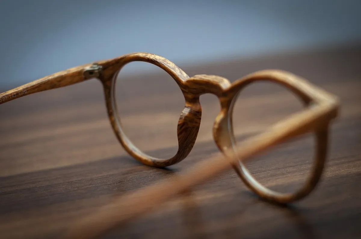 Round eyeglasses with a wood-grain frame resting on a dark wooden surface