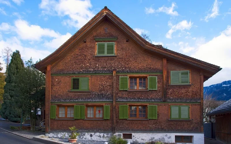 Wood-shingled house facade with a weathered reddish-brown exterior finish Wood-shingled house facade with a weathered reddish-brown exterior finish