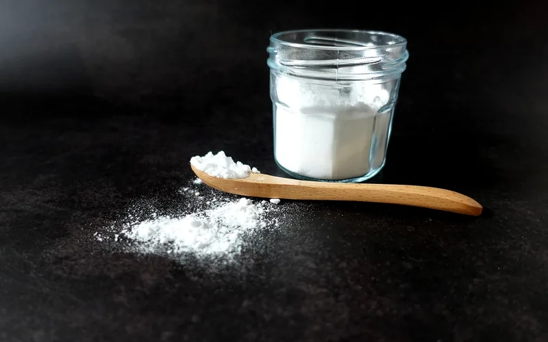 Jar of baking soda powder with a wooden spoon, the natural cleaner often mistakenly used on wood floors